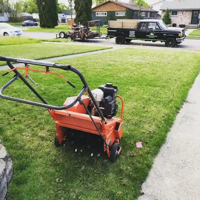 An orange core aerator parked on a lawn beside a sidewalk