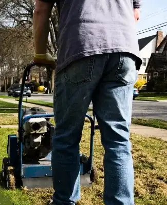 Dethatcher making a pass over a lawn, operator's legs visible