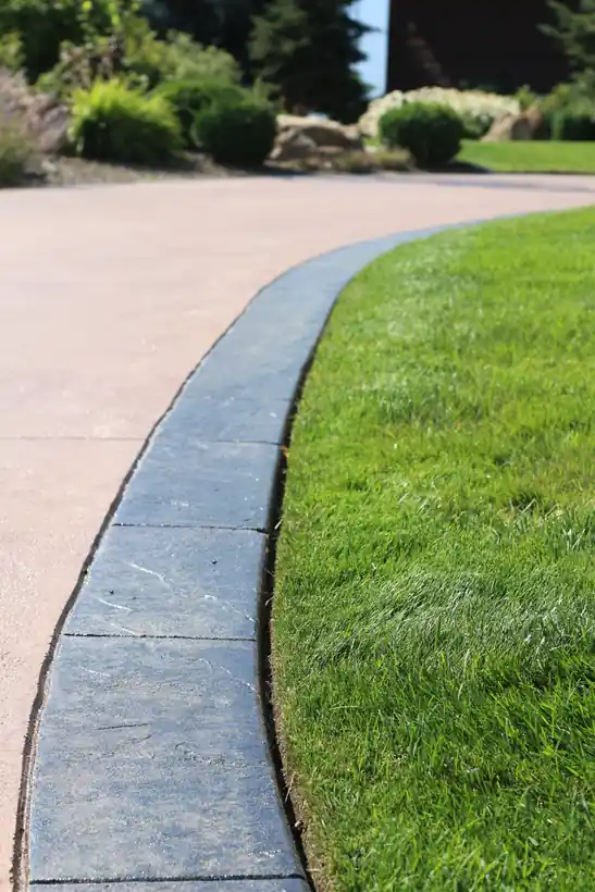 A freshly edged lawn curving along a charcoal stamped-concrete curb beside a driveway