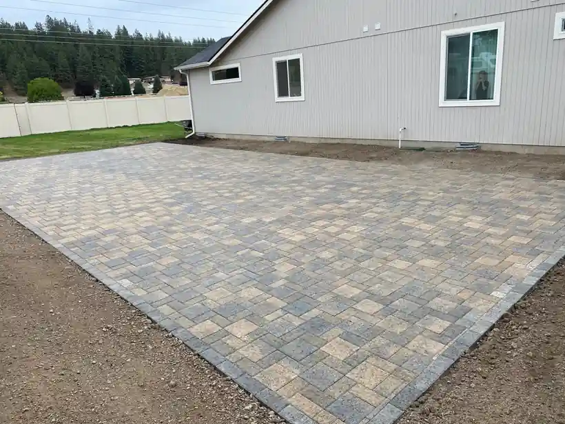 A large new paver pad laid beside a grey house