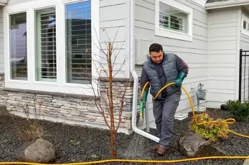 A technician spraying a rock bed beside a house
