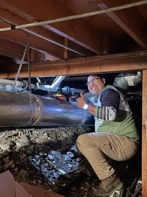 Technician in a branded jersey working on a line in a crawlspace