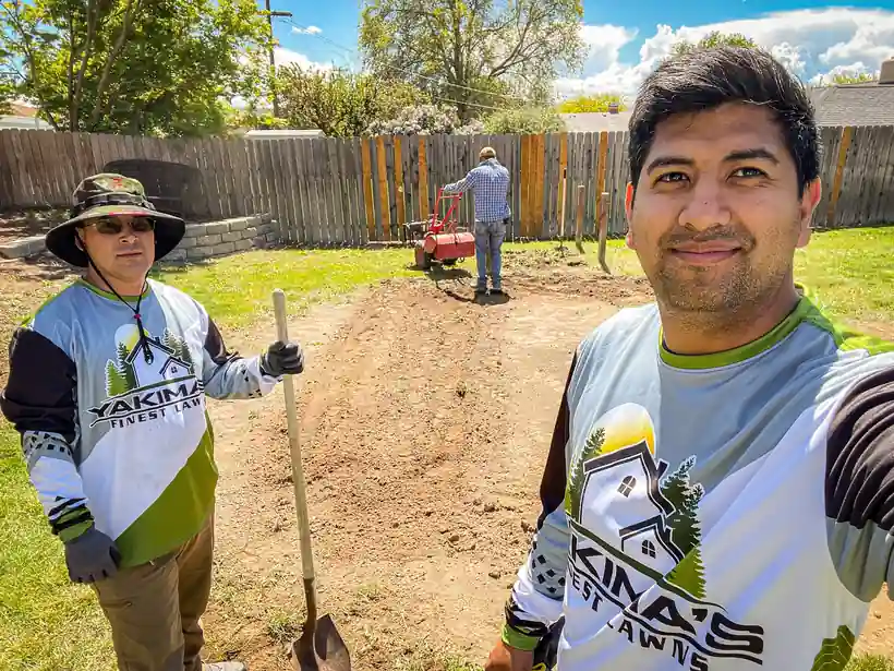 Two Yakima's Finest Lawns crew members in green and white company jerseys on a graded yard before sod goes down