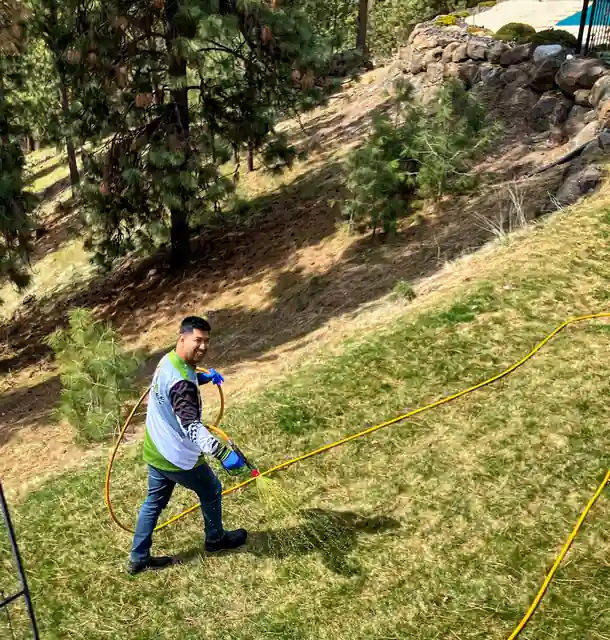 A technician spraying a steep grass slope with a hose reel line
